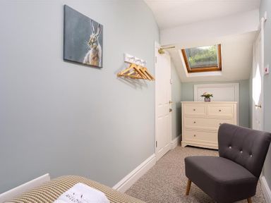 A small room with a gray chair a cream dresser a skylight window and a painting of a rabbit on the wall at Highbank in Bowness