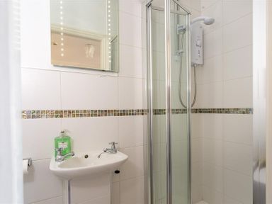 A small bathroom with a sink, mirror, soap dispenser, and a shower enclosure with a glass door at Highbank in Bowness