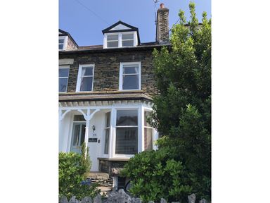 Stone house with white framed windows and green bushes in front at Highbank in Bowness