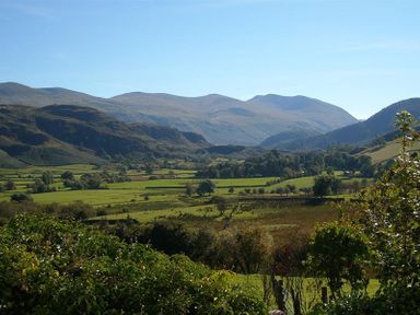 A rural landscape with fields trees and hills under a clear sky at Nest Barn in Keswick