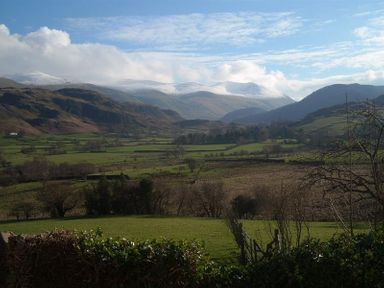 A rural landscape with fields and hills with snow capped mountains in the background at Nest Barn in Keswick