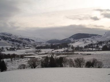 A snow-covered rural valley with hills and scattered trees at Nest Barn in Keswick