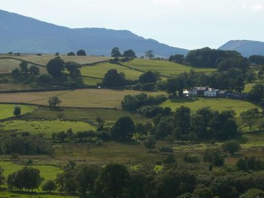 A rural landscape with green fields trees and a farmhouse at Nest Barn in Keswick