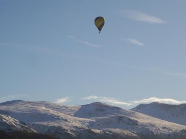 A hot air balloon flying above snow covered mountains under a clear sky at Nest Barn in Keswick