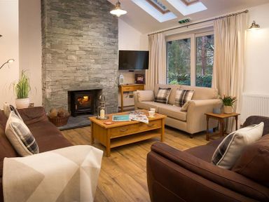 A living room with two brown sofas a beige sofa a wooden coffee table and a stone fireplace at Lanterns At Grasmere in Grasmere