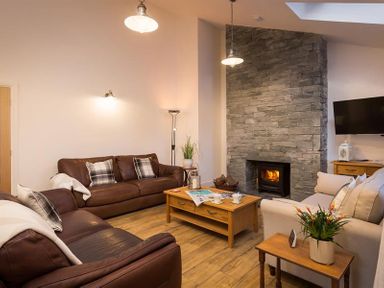 A living room with leather sofas wooden coffee tables a stone fireplace and a wall-mounted television at Lanterns At Grasmere in Grasmere