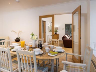 A dining room with a wooden table set for breakfast and white chairs at Lanterns At Grasmere in Grasmere