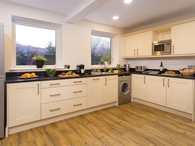 A kitchen with white cabinets black countertops wooden floor and two windows at Lanterns At Grasmere in Grasmere