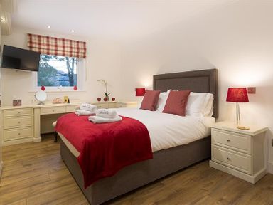 A bedroom with a double bed with red pillows and blanket bedside tables with lamps and a window with a checked blind at Lanterns At Grasmere in Grasmere
