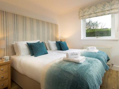 A bedroom with two single beds with teal cushions and blankets next to a window at Lanterns At Grasmere in Grasmere