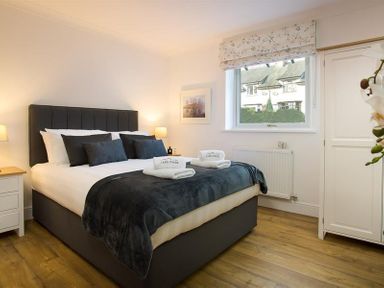 A bedroom with a bed black headboard bedside tables lamps window and white wardrobe at Lanterns At Grasmere in Grasmere