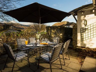 An outdoor patio with a dining table and six chairs under a large umbrella at Lanterns At Grasmere in Grasmere