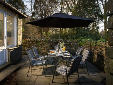 An outdoor dining area with a table set for six under a large umbrella surrounded by a stone wall at Lanterns At Grasmere in Grasmere