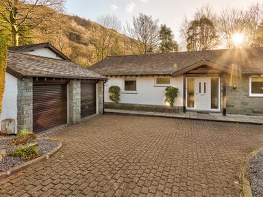 An exterior view of a single-story house with a double garage paved driveway and trees in the background at Lanterns At Grasmere in Grasmere