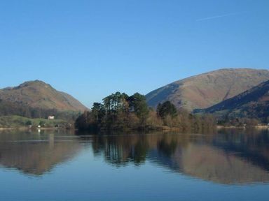 A lake with trees on an island and hills in the background at Lanterns At Grasmere in Grasmere