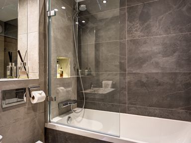A bathroom with a bathtub shower combination glass partition mounted on the bathtub with toiletries on built-in shelves and toiletry bottles on a counter at Hart Head Barn in Rydal