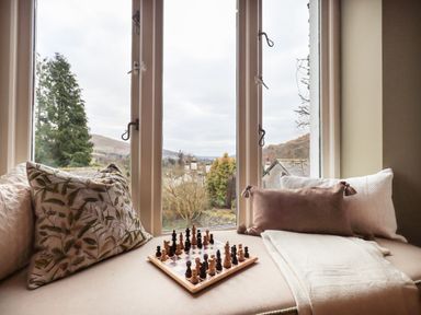 A window seat with cushions a blanket and a chessboard by a window at Hart Head Barn in Rydal