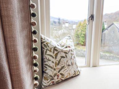 A window with a floral patterned cushion on the sill and a curtain with pom poms at Hart Head Barn in Rydal