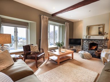 A living room with a stone fireplace a TV a wooden coffee table and armchair at Hart Head Barn in Rydal