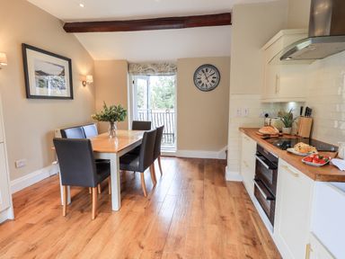 A kitchen and dining area with a wooden table and black chairs next to a window and white cabinets with a wooden countertop at Hart Head Barn in Rydal