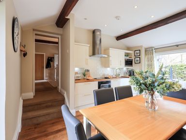 A kitchen and dining area with wooden table and black chairs and a vase with flowers at Hart Head Barn in Rydal