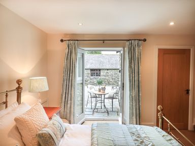 A bedroom with a brass bed frame lampshade bedside table open doors to a patio with a table and chairs at Hart Head Barn in Rydal