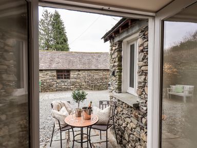 A stone patio with a small round table holding a plant and champagne bucket surrounded by two chairs at Hart Head Barn in Rydal