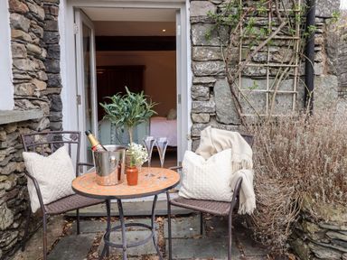 A small outdoor seating area with two chairs and a round table with a champagne bottle and glasses at Hart Head Barn in Rydal