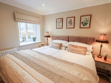 A bedroom with a bed two bedside tables lamps and flower artwork on the wall at Hart Head Barn in Rydal