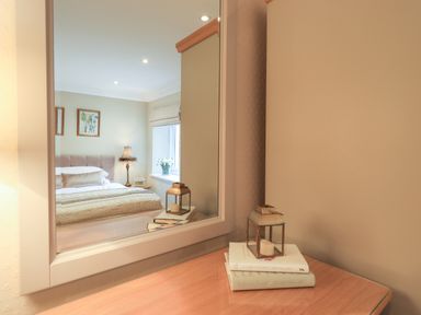 A bedroom reflected in a mirror showing a bed bedside table with lamp and window with flowers at Hart Head Barn in Rydal
