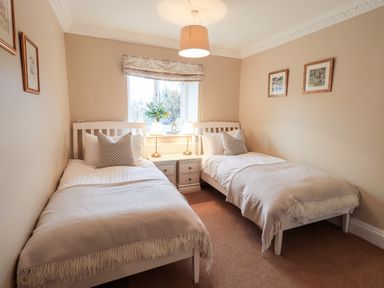 A bedroom with two single beds a window between them and bedside table with lamps at Hart Head Barn in Rydal
