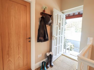 An entrance hallway with a wooden door a white door open to outside boots on the floor and a coat rack with jackets and a hat at Hart Head Barn in Rydal