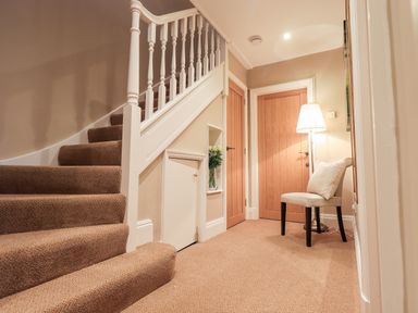 A carpeted stairway next to two wooden doors with a chair and floor lamp in a hallway at Hart Head Barn in Rydal