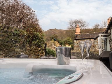 A hot tub with a champagne bottle in an ice bucket and two glasses outside a stone cottage at Hart Head Barn in Rydal