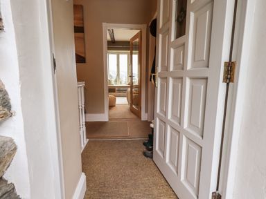 A hallway with a partially open white door leading to a room with windows at Hart Head Barn in Rydal