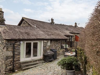 An outdoor patio area with stone walls stone steps a barbecue grill a dining table with chairs and a potted plant at Hart Head Barn in Rydal