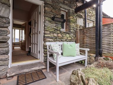 A white bench with cushions outside a stone building with an open door at Hart Head Barn in Rydal