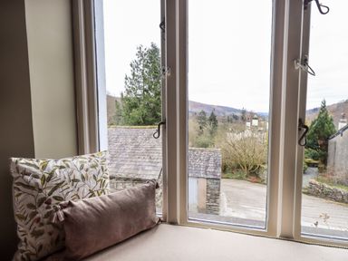 A window seat with two cushions overlooking a stone roof and trees at Hart Head Barn in Rydal