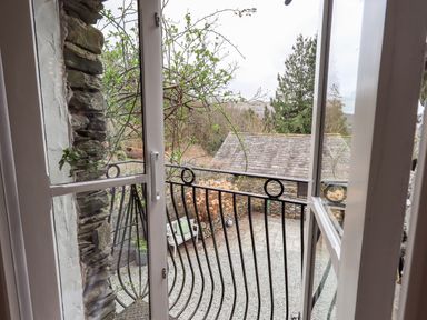 View through glass door of small balcony with metal railing overlooking stone patio and garden at Hart Head Barn in Rydal