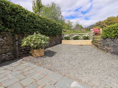 A gravel driveway with stone walls and wooden planters with plants at Hart Head Barn in Rydal
