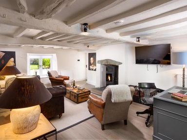 A living room with a fireplace a television a desk with a chair and leather armchairs at Underhowe in Grasmere