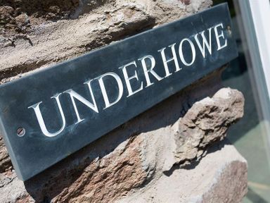 A close up of a sign reading Underhowe attached to a stone wall at Underhowe in Grasmere