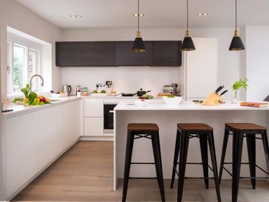 A kitchen with white cabinets a countertop island with stools and hanging lights at Underhowe in Grasmere