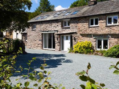Stone house with white doors and windows surrounded by plants and gravel yard at Underhowe in Grasmere
