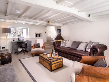 A living room with a brown leather sofa a wooden chest as coffee table two armchairs a grey desk with a computer and a floor lamp at Underhowe in Grasmere