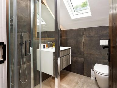 A bathroom with a glass shower enclosure a white sink and vanity a toilet and a skylight window at Underhowe in Grasmere