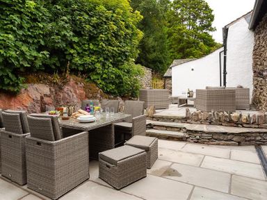 An outdoor patio with a dining table set and seating area with chairs and stools at Underhowe in Grasmere