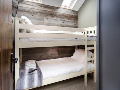 A small bedroom with cream bunk beds and a wooden paneled wall at Underhowe in Grasmere