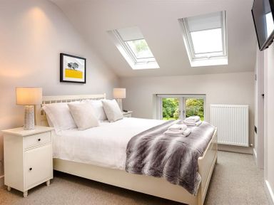 A bedroom with a bed white pillows bedside tables lamps skylights and a wall-mounted television at Underhowe in Grasmere