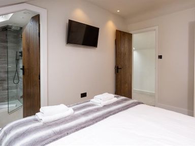 A bedroom with a bed and folded towels on a blanket a wall-mounted tv and two wooden doors one leading to a bathroom at Underhowe in Grasmere